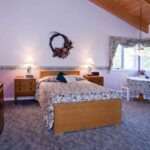 Bedroom with light colored walls, carpeting, light wooden bed, multicolored floral wedding, antique wooden dresser, and sitting area